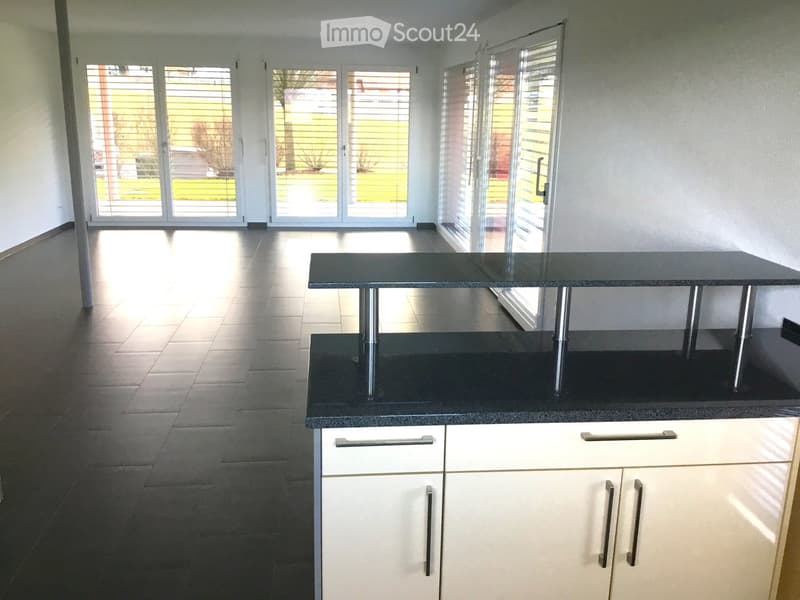 Modern kitchen with white cabinets, black countertop, and a sleek black table with metal legs. Large windows and sliding doors provide natural light and access to the outdoor area.