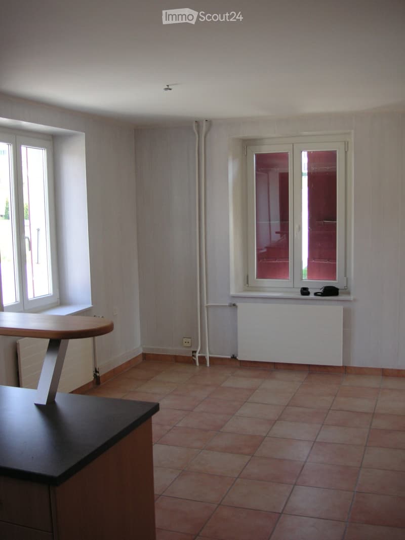 Empty room with tiled floor, white walls, and two windows. A small round table is positioned near the left wall.