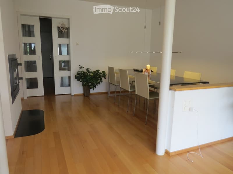 Open-plan living and dining area with light wooden flooring, a dining table with chairs, a potted plant, and a candle on the table.