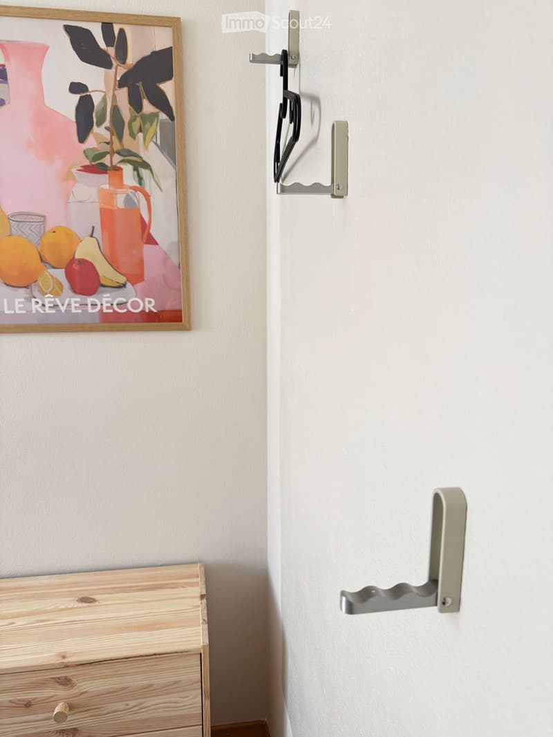A hallway with a wooden chest of drawers, a framed painting on the wall, and a modern door handle.