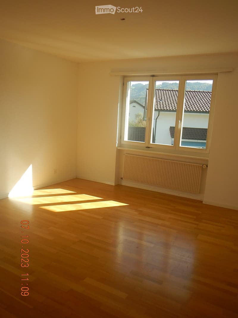 Empty room with wooden flooring, large windows, and a radiator under the windows.