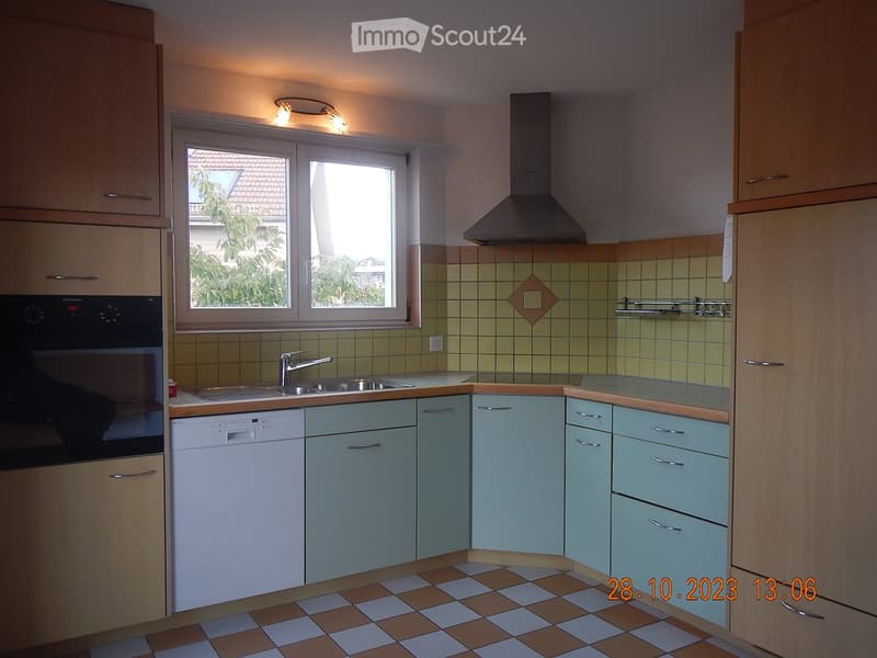 A well-lit kitchen with light green cabinets, a stainless steel sink, a white dishwasher, and a black oven. The backsplash features a diamond-shaped tile design, and the floor has a checkered tile pattern.