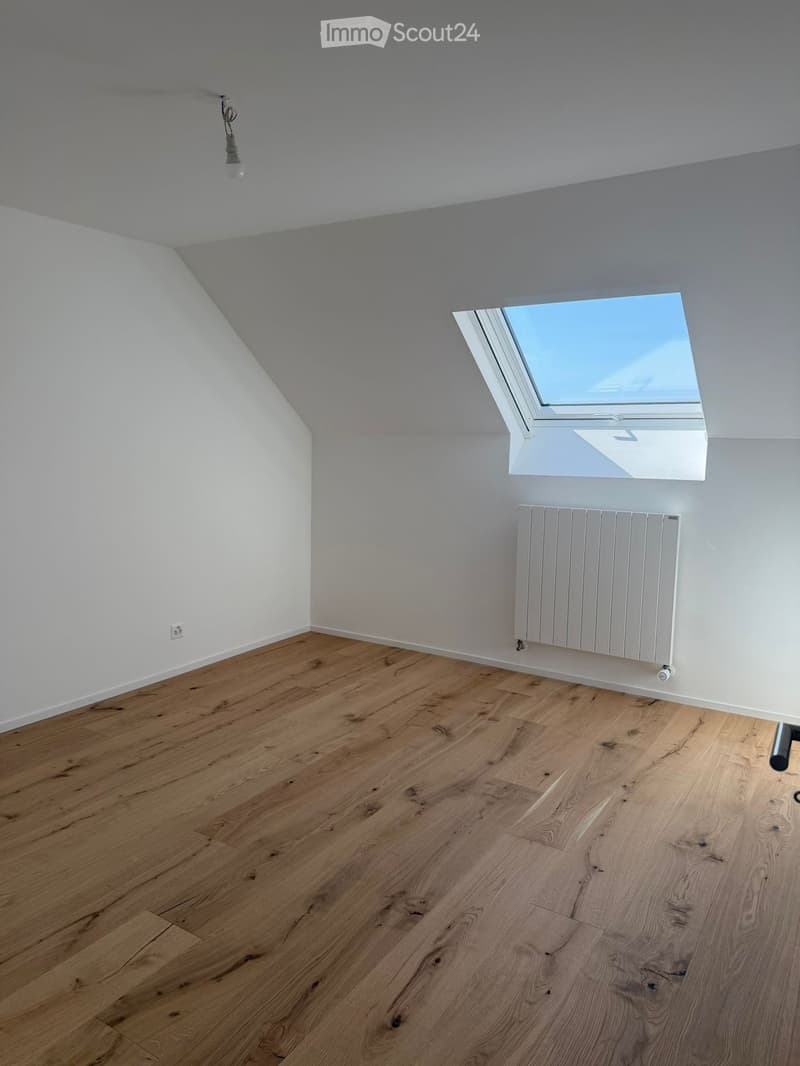 Empty room with wooden flooring, white walls, a skylight window, and a radiator. No furniture or equipment is present.