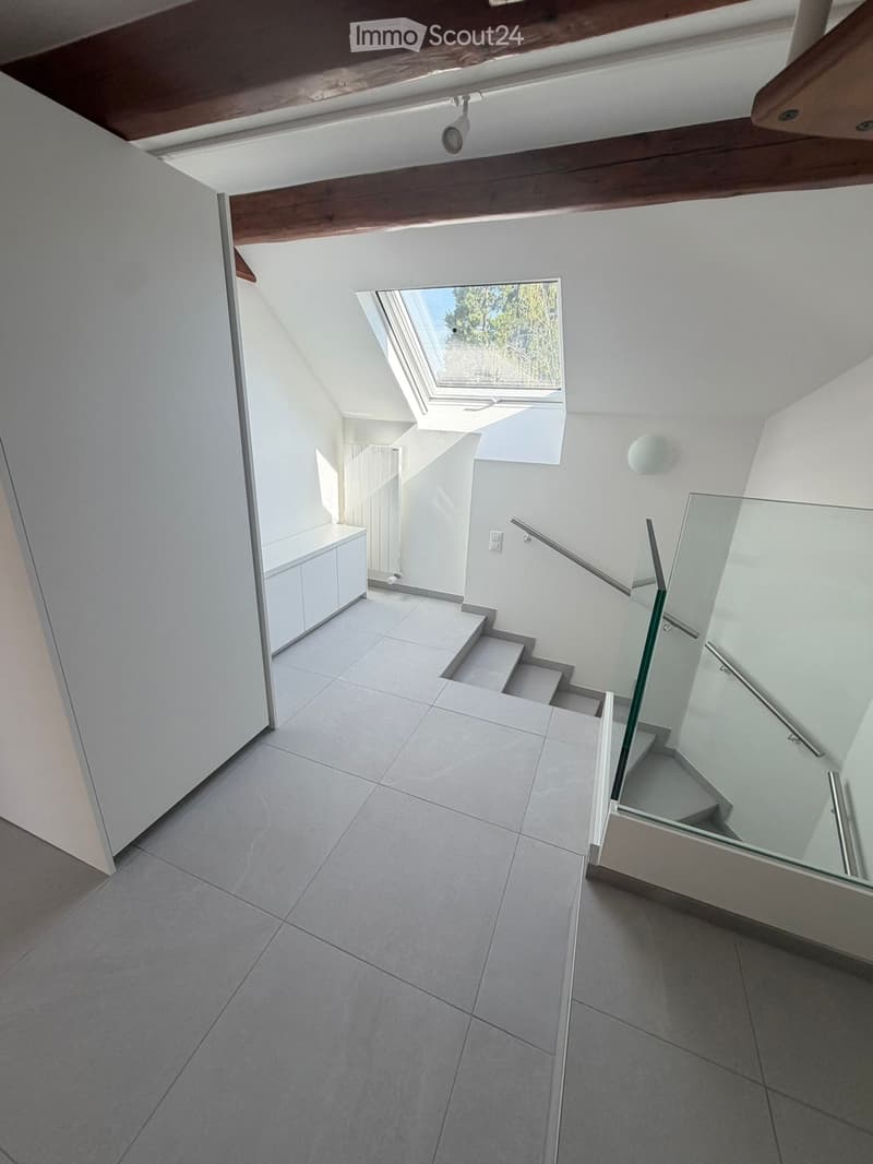 Modern hallway with tiled floors, white walls, glass staircase railing, and skylight window at the top.