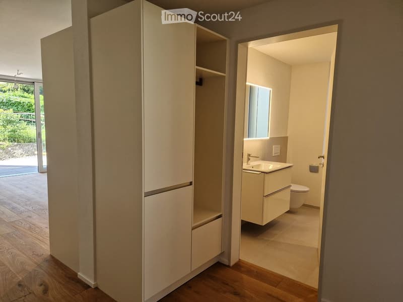 Modern bathroom with a white sink, toilet, and built-in cabinet. The room features light-colored tiles and a large mirror above the sink.