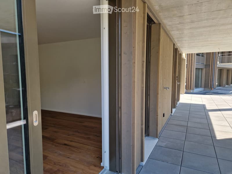 Empty hallway with wooden flooring and tiled section, featuring glass doors and wooden paneling.