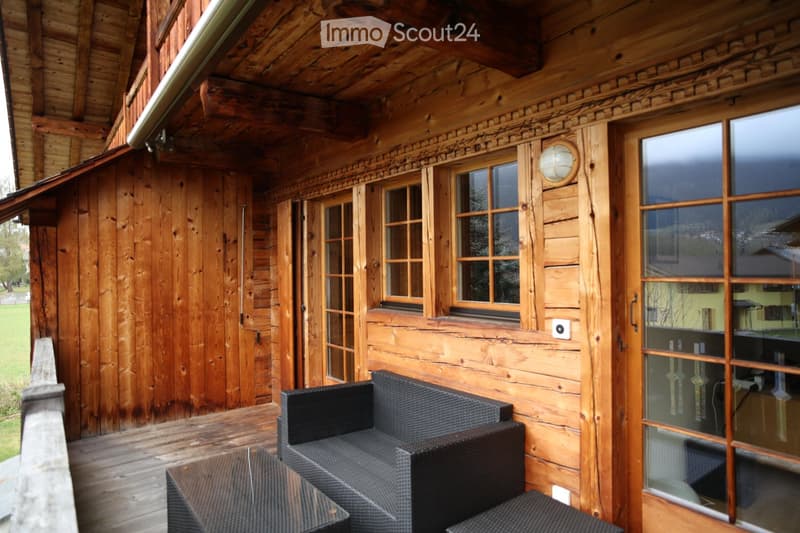 Wooden balcony with large windows, black wicker sofa and table, scenic view.