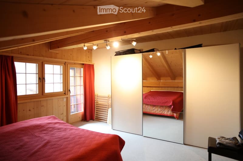 Cozy wooden bedroom with exposed beams, large windows, and a sliding mirror that reveals a second bed in a lofted area.