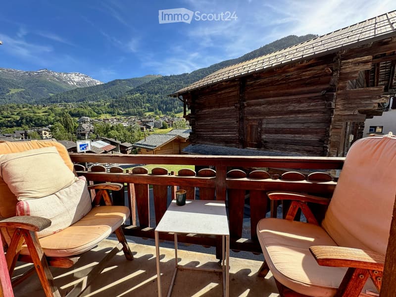 Balcony with two chairs and a small table, overlooking a scenic mountain view and village.