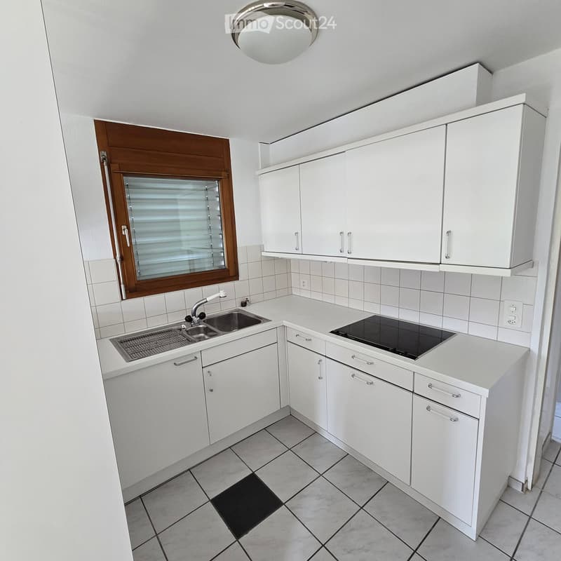 Modern kitchen with white cabinets, a sink, and an electric stove, featuring tiled walls and floor.