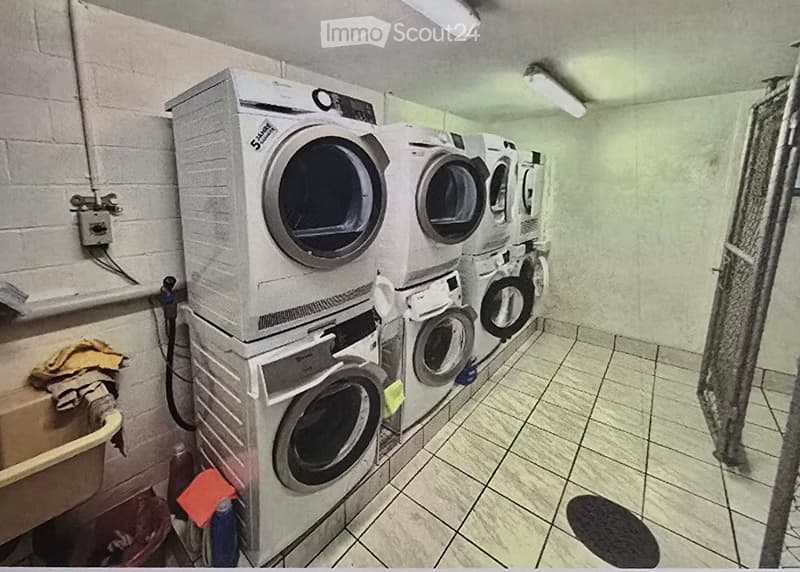 A small utility room with a stacked washing machine and dryer unit, tiled floor, and brick walls.