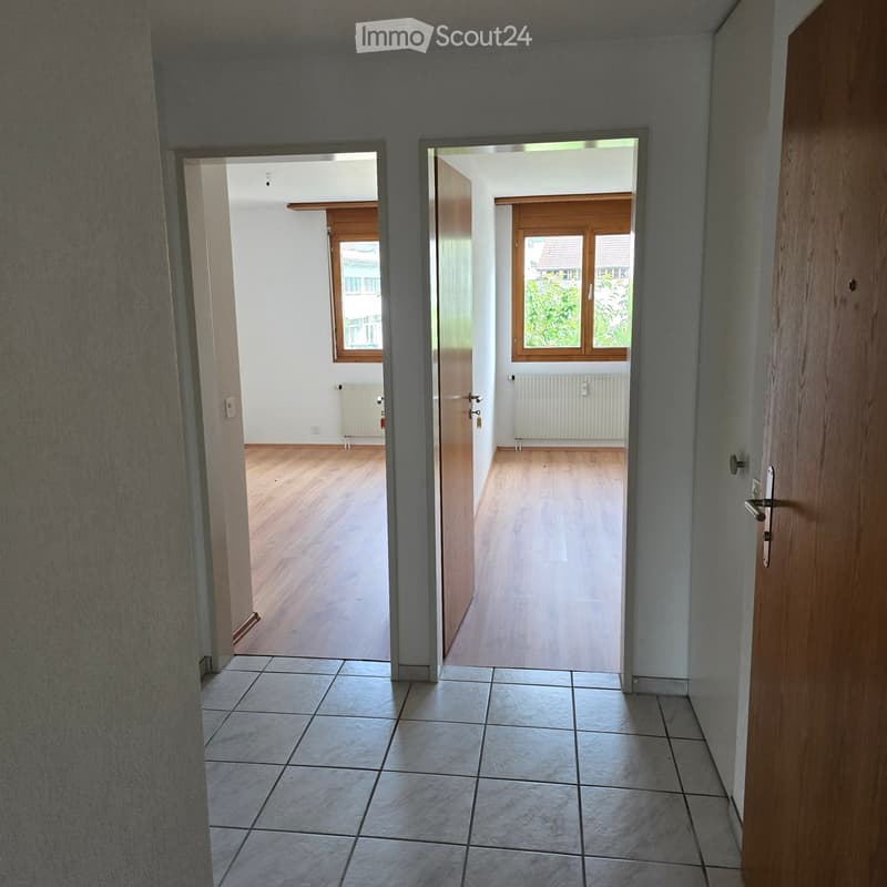 Empty hallway with tiled floor and wooden doors leading to rooms with wooden flooring and windows.