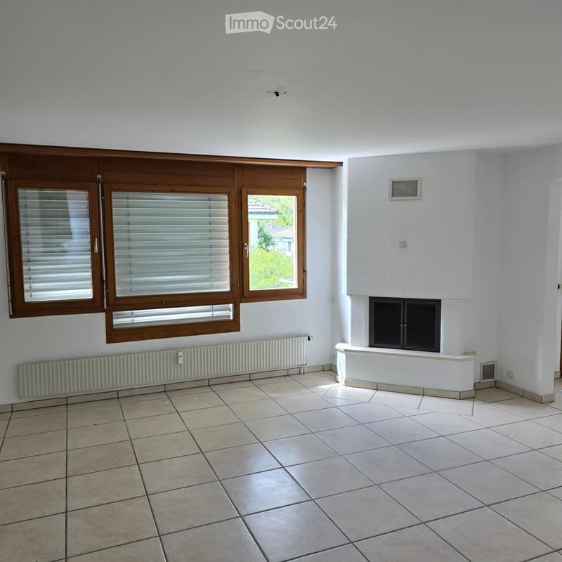 Empty room with tiled floor, white walls, large windows with blinds, fireplace, and radiators.