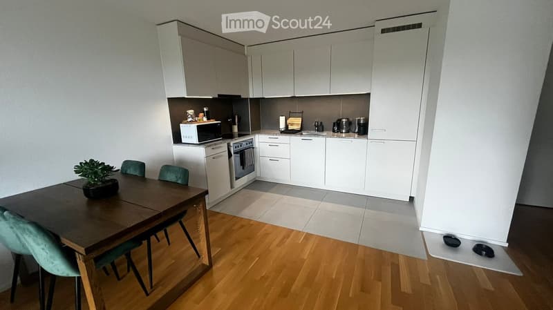 Modern kitchen with white cabinets, a wooden dining table with chairs, and various appliances including a microwave, oven, and dishwasher.