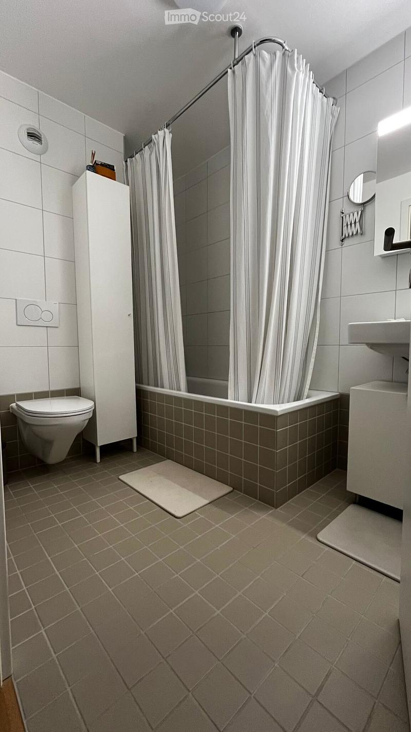Modern bathroom with a bathtub, toilet, sink, and shower curtain. Features tiled walls and floor, a white cabinet, and a mirror above the sink.