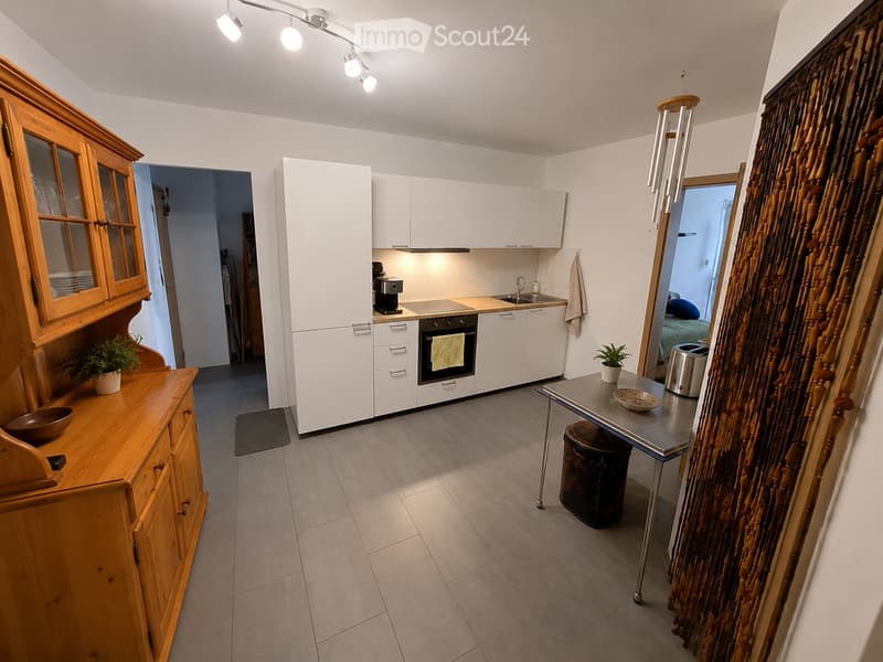 Modern kitchen with white cabinets, wooden sideboard, stainless steel appliances, and a small dining area.