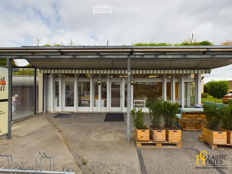 Outdoor seating area with a covered patio, glass doors leading to an interior space, potted plants, and a small wooden table with chairs.