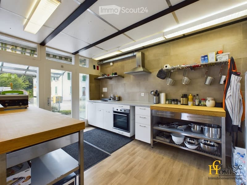Modern kitchen with white cabinets, stainless steel appliances, wooden island, and ample natural light from large windows and skylights.