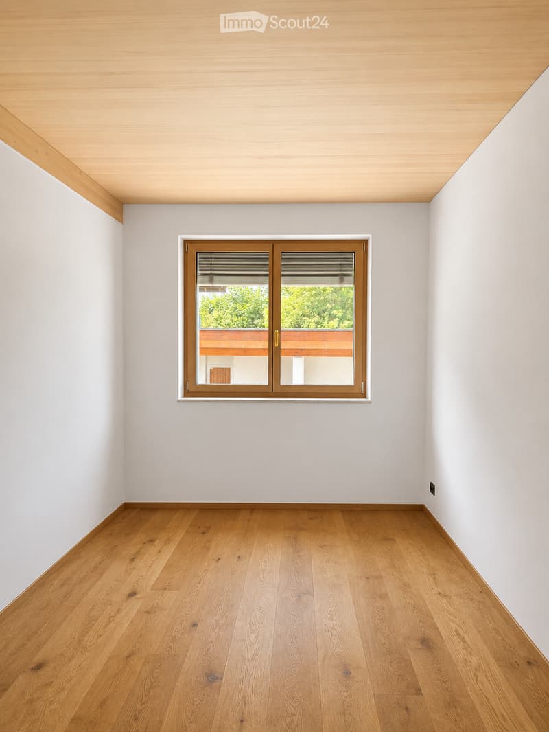 Empty room with light wooden flooring, white walls, and a large window with blinds. The ceiling is also made of light wood.
