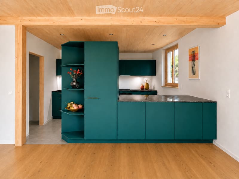 Modern kitchen with teal cabinets, wooden ceiling, and light wooden flooring. Features a countertop with a vase of flowers and a bowl of fruit.