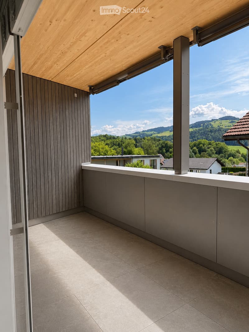 Modern balcony with wooden ceiling, tiled floor, grey walls, and a panoramic view of a green landscape.