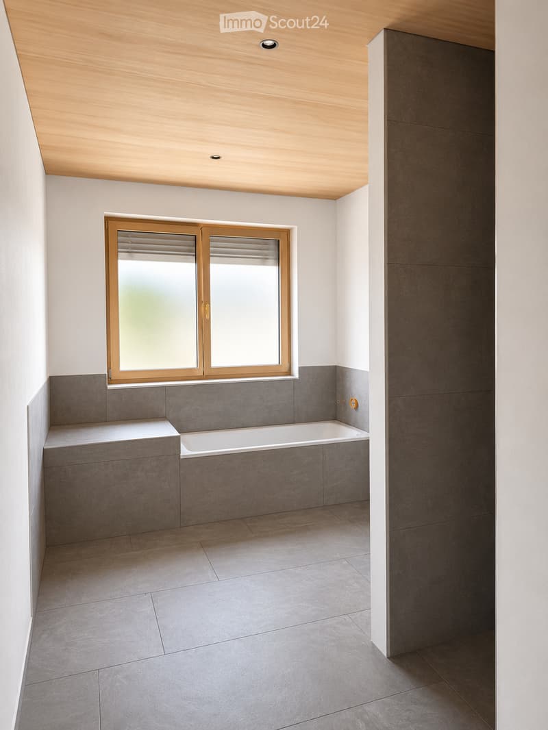 Modern bathroom with a bathtub, grey tiled walls and floor, large window with blinds, and a wooden-framed window.