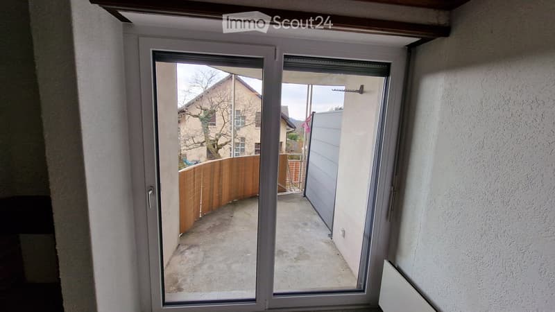 Sliding glass doors open to a small concrete balcony area with a wooden fence and a view of neighboring houses.