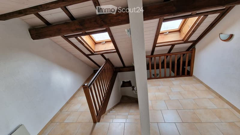 Staircase with wooden railings and skylights, beige tiled floor, white walls, exposed wooden beams on the ceiling.