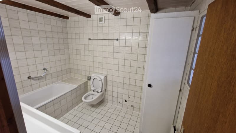 Bathroom with white tiled walls and floor, a bathtub, a toilet, and a wooden door.