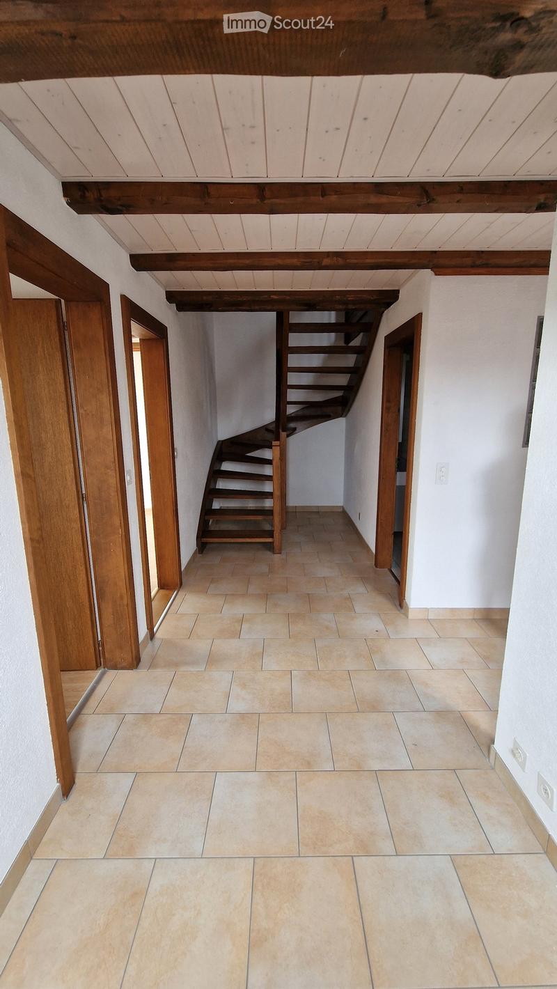 Empty hallway with tiled floor, wooden doors, and a staircase leading upwards.
