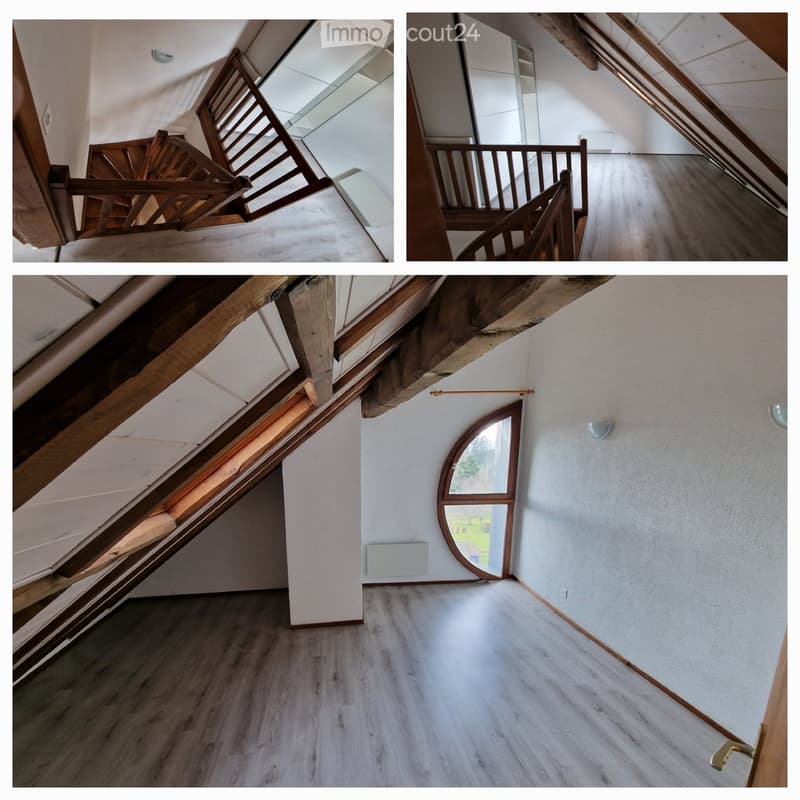 Empty attic space with wooden beams, wooden staircase, and a round window offering a view of the outdoors.
