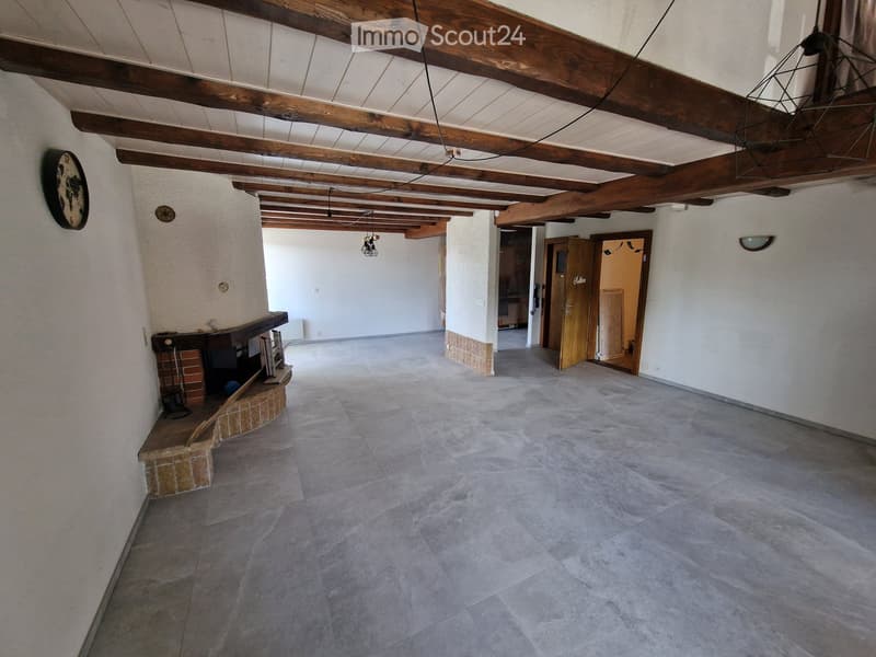 Empty room with exposed wooden beams, tiled floor, and a small brick fireplace area. No furniture or equipment present.