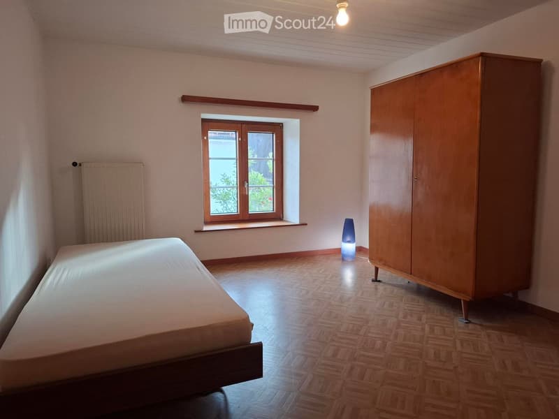 Bedroom with wooden floor, bed, wardrobe, and a small lamp near the window.