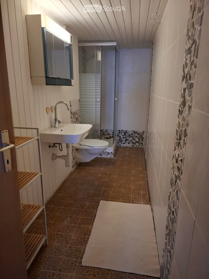 Modern bathroom with a white sink, chrome faucet, toilet, mirrored cabinet, and a glass-enclosed shower area with mosaic tiles.