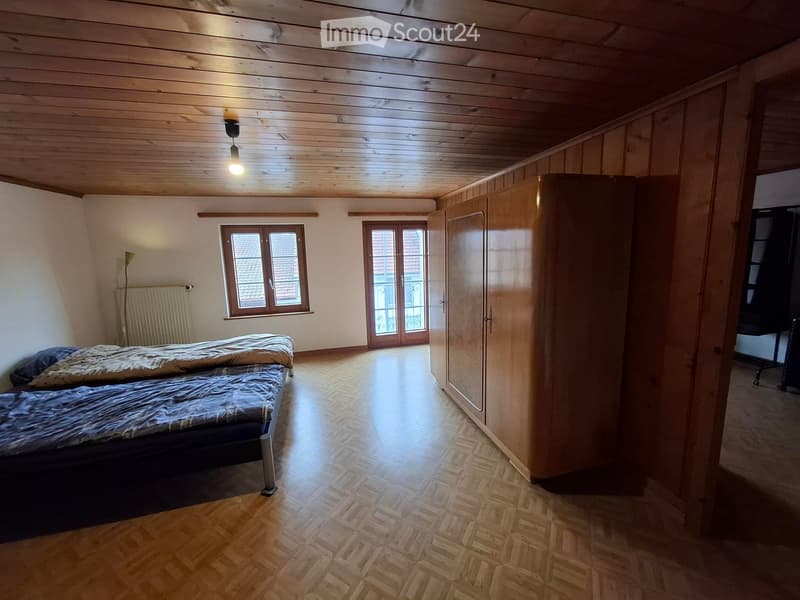 Bedroom with wooden floor, bed, wardrobe, radiator, and floor lamp. Features a window and a door leading to a balcony.