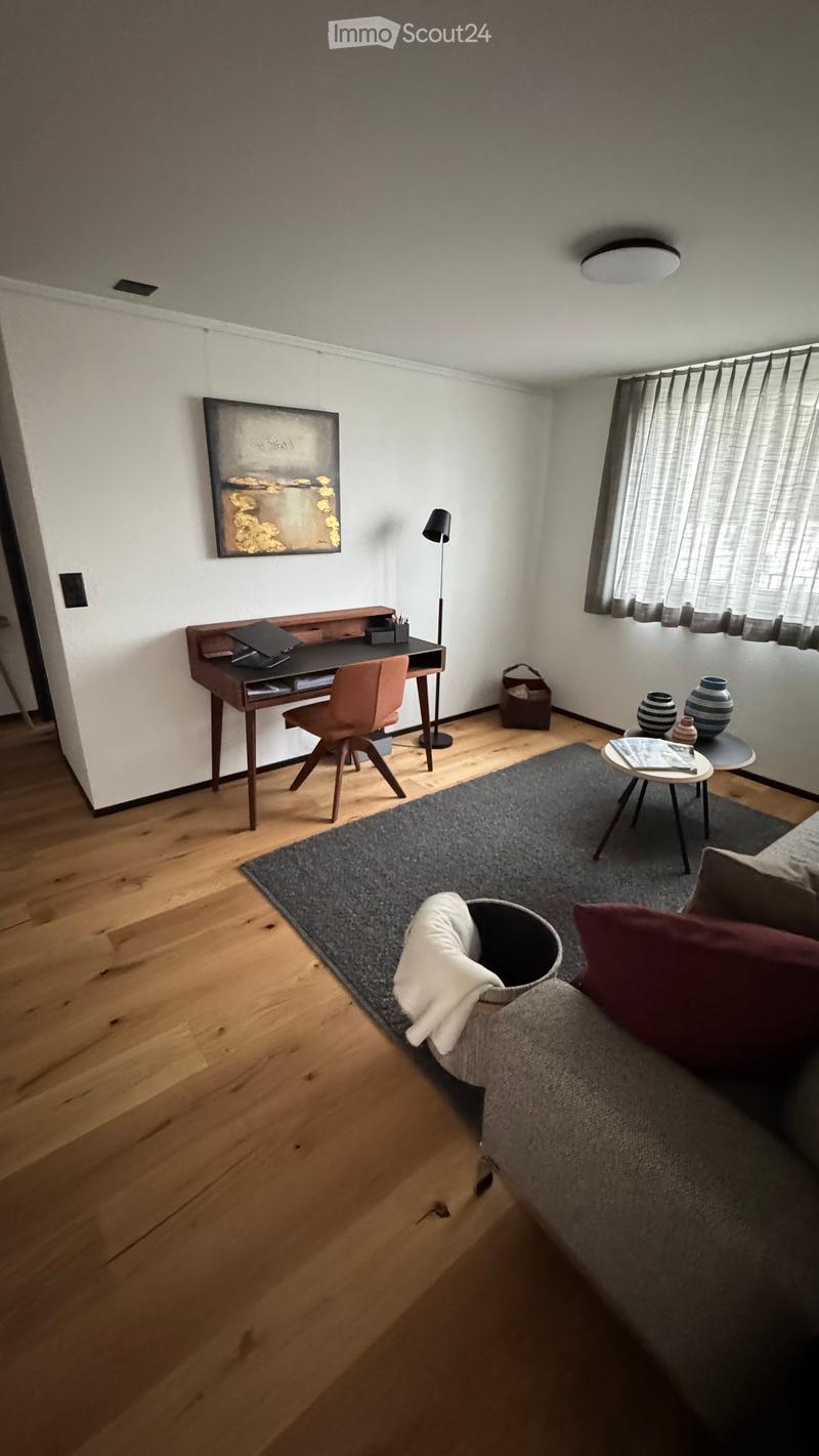 Modern living room with wooden flooring, a grey sofa, coffee table, desk with laptop, and decorative vases.