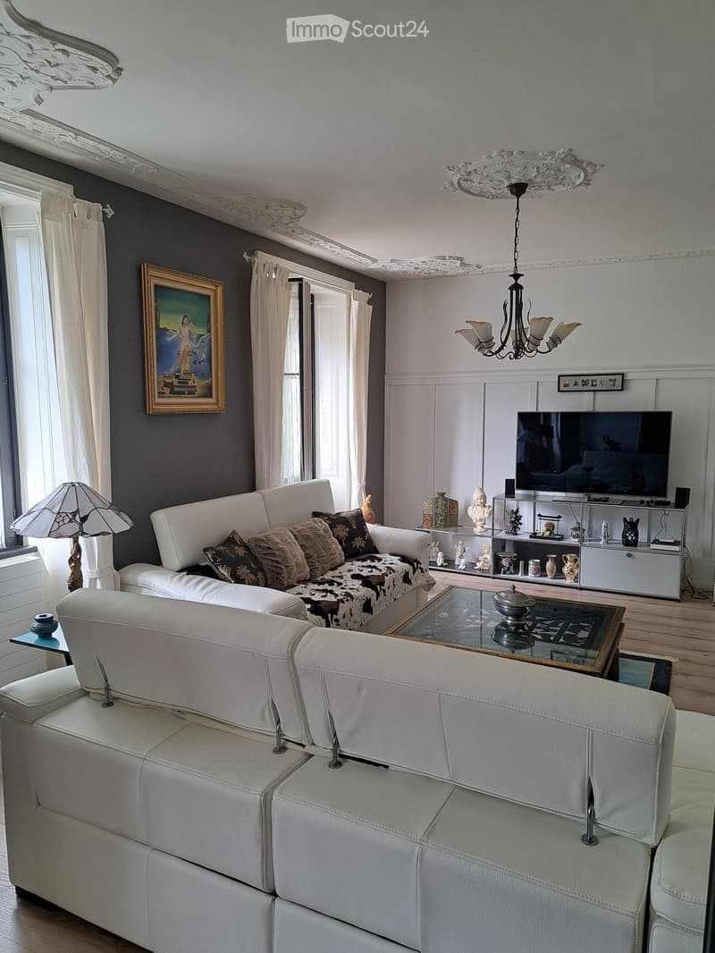 Elegant living room with white leather sofa, glass coffee table, decorative cabinet, and ornate chandelier.
