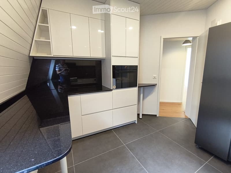 Modern kitchen with white cabinets, black countertops, and a built-in oven. The space features grey tiled flooring and a sleek, contemporary design.