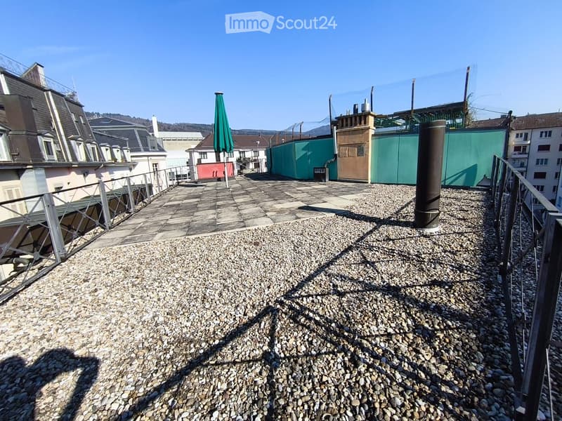 Rooftop terrace with gravel surface, metal railing, and a closed umbrella in the background.