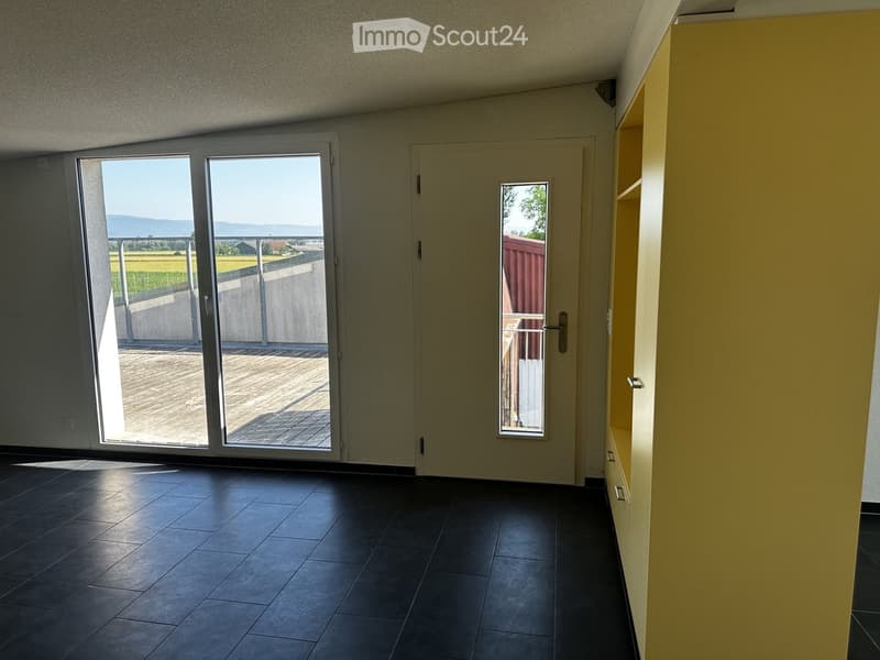 Empty room with dark tiled floor, large sliding glass doors leading to a balcony, and a small window with a view of the outdoor area.