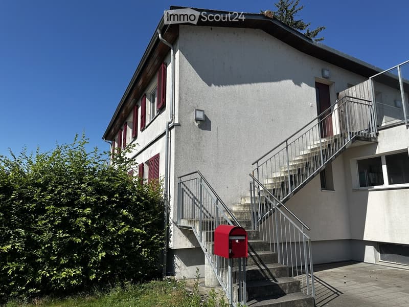 Two-story house with red shutters, a staircase leading to a balcony, and a red mailbox.
