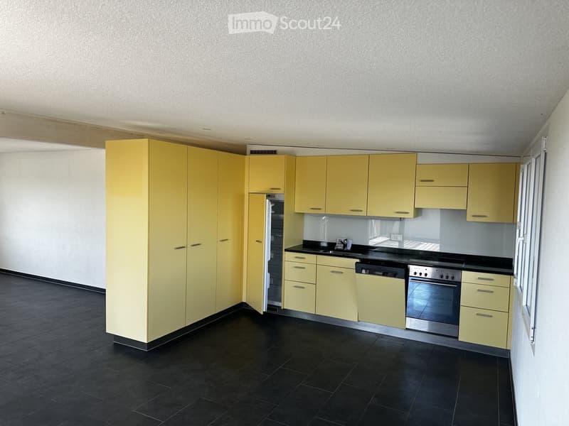 Modern kitchen with yellow cabinets, black countertops, and stainless steel appliances including a refrigerator, dishwasher, and oven. The floor is black tiled.
