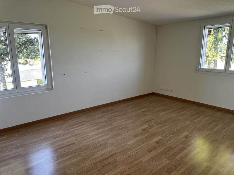 Empty room with wooden flooring and white walls, featuring two windows with white frames and visible electrical outlets on the wall.