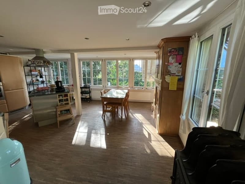 Bright, open-plan kitchen and dining area with wooden flooring, large windows, a dining table with chairs, a kitchen island, and built-in cabinets.