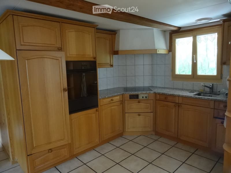 Well-lit kitchen with wooden cabinets, granite countertops, tiled floor, and a window above the sink.