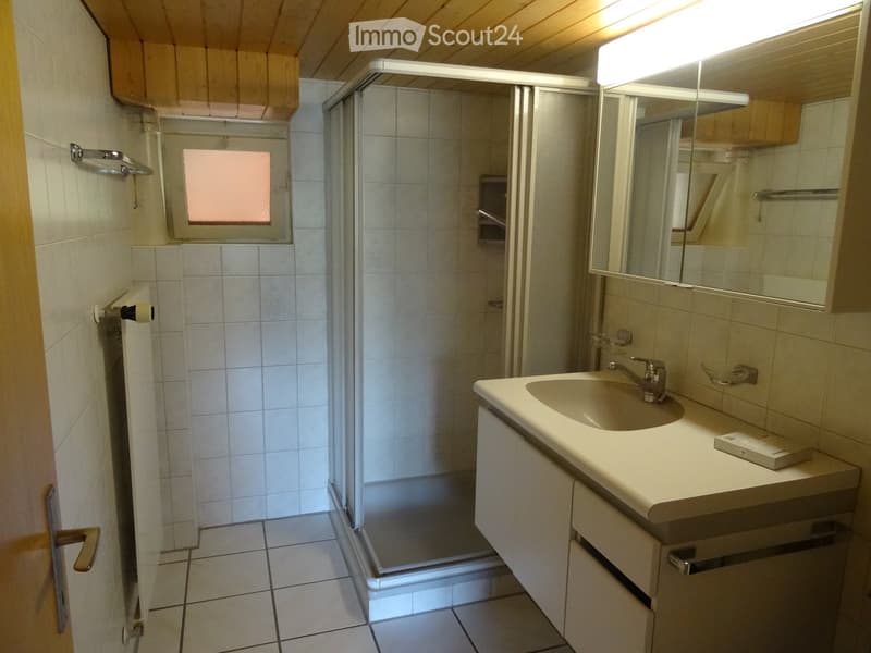 Bathroom with a sink, mirror, cabinet, and a glass-enclosed shower. The room features tiled walls and floor, a window above the shower, and a small light fixture above the mirror.