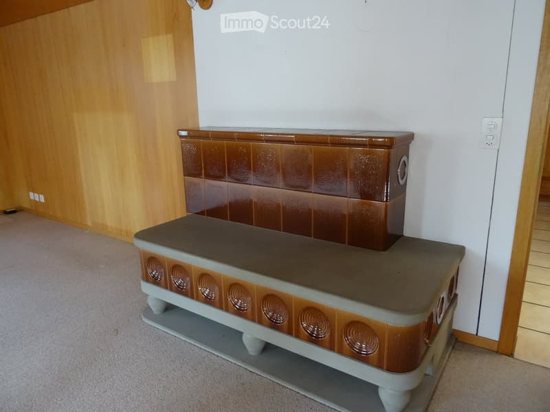 Empty room with a tiled fireplace and a grey bench, wooden walls, and carpeted floor.