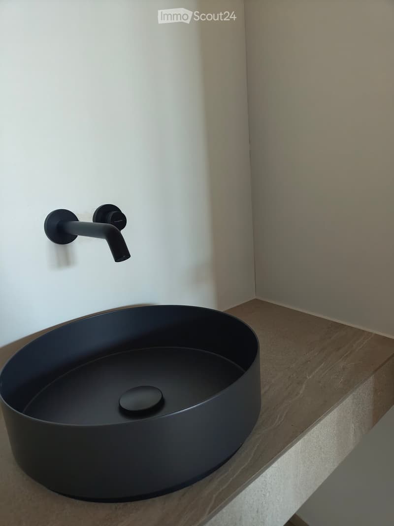 Modern bathroom sink with a sleek, dark grey basin and a minimalist black faucet mounted on the wall.