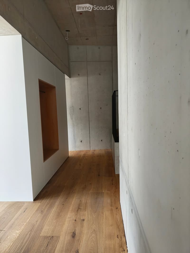 Minimalist hallway with light wooden flooring, white concrete walls, and a built-in wooden shelf on the left side.