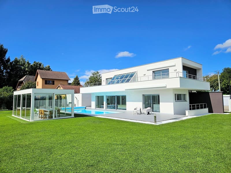 Modern two-story house with white facade, large windows, balcony, swimming pool, and outdoor seating area.